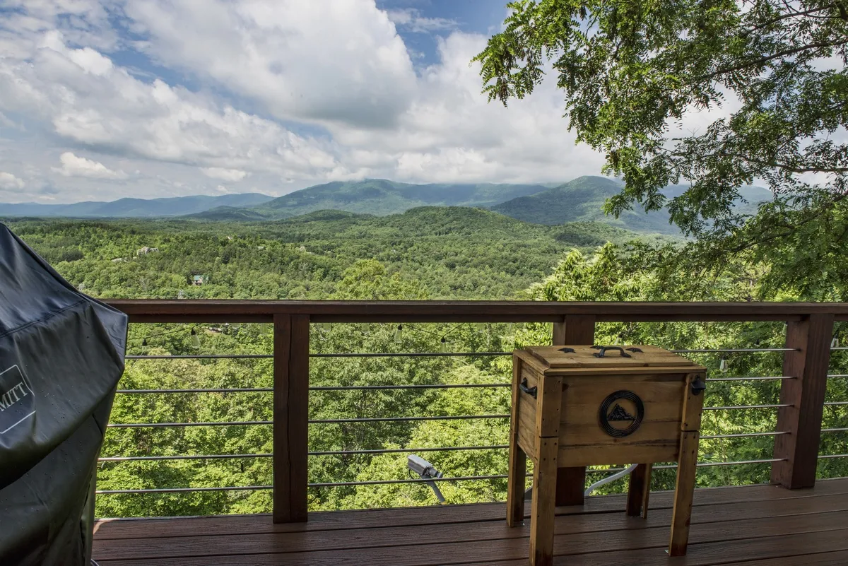 A tranquil deck scene featuring a classic wooden cooler and deck railing, with a sweeping mountain view beyond. The setting hints at leisure activities such as outdoor dining, relaxing, or simply gazing at the scenery, inviting guests to appreciate the peace and natural beauty.