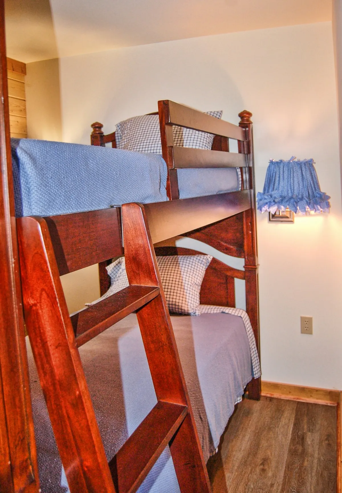 A cheerful bunk bed with blue bedding and a sturdy ladder stands against the wall, lit warmly by a decorative lamp. The playful arrangement invites both rest and imaginative play for younger guests.