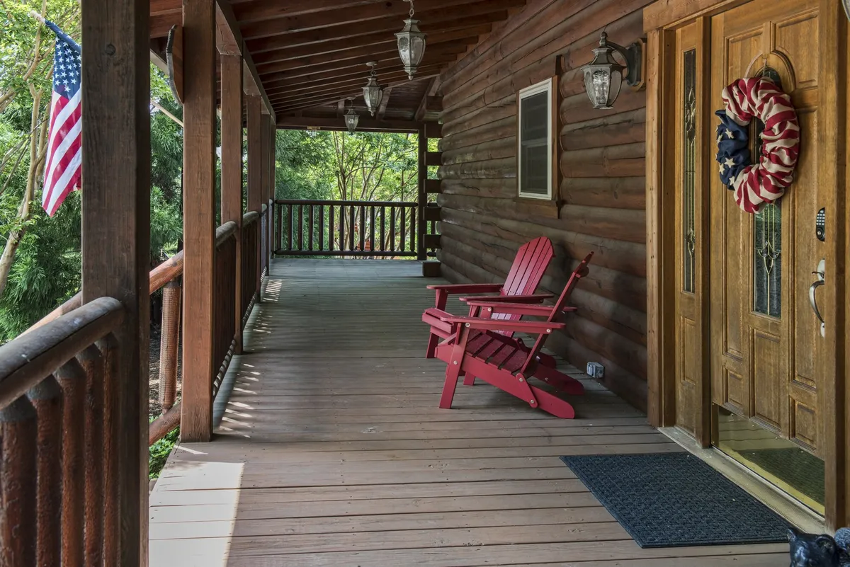 This exterior image features a welcoming front porch with a red wooden chair, an American flag, lanterns, and a festive wreath on the front door. The scene feels inviting and warm, set against a backdrop of natural surroundings, signaling a perfect spot to greet guests or relax with loved ones.