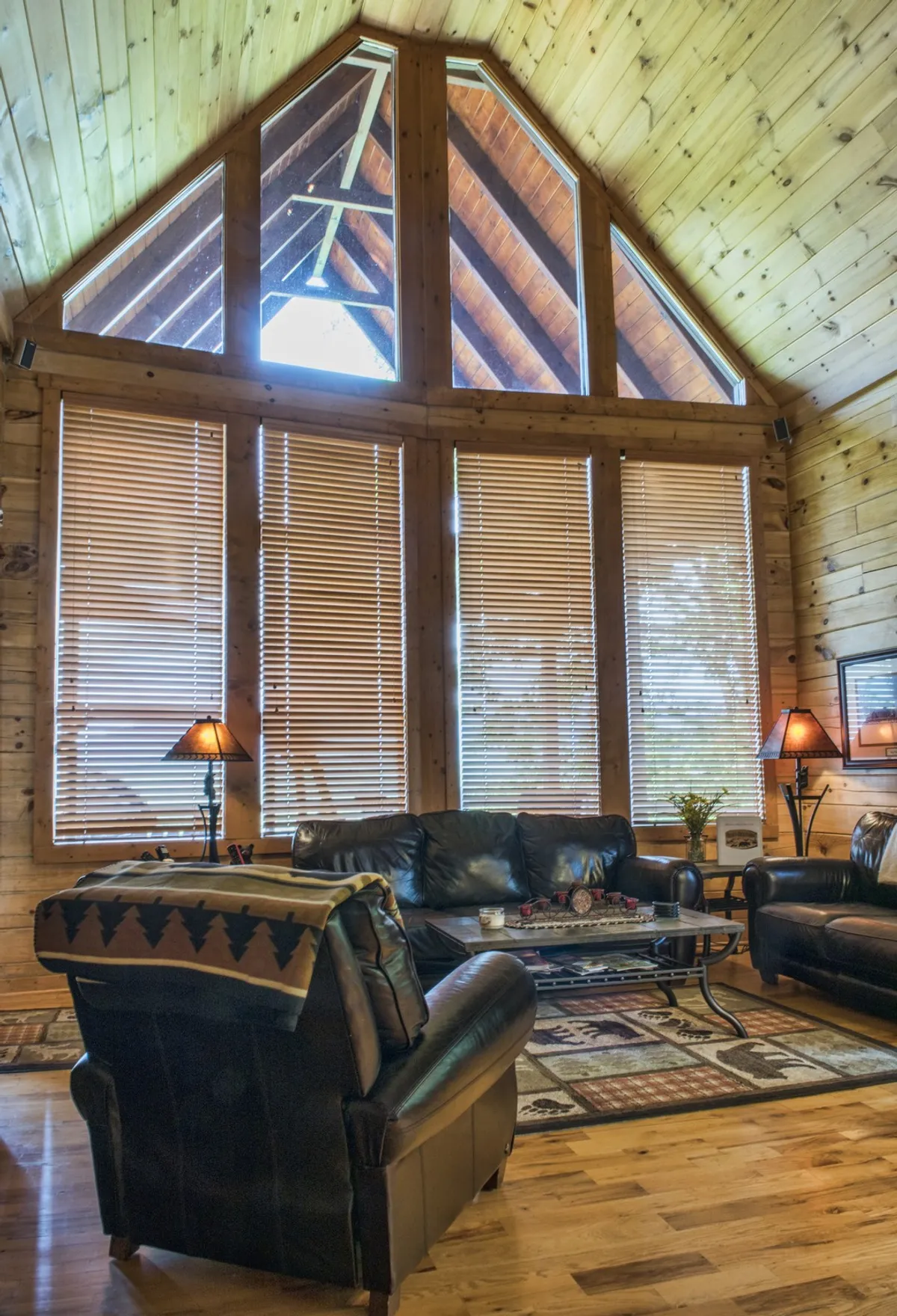 A spacious living room filled with natural light from large windows. The room features plush leather sofas arranged around a coffee table atop a decorative rug, with a fireplace in view, creating a warm and welcoming environment perfect for family gatherings, relaxation, and intimate conversations.